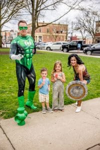 Volunteers dressed as Green Lantern and Wonder Woman pose with a young boy and girl eating frozen treats