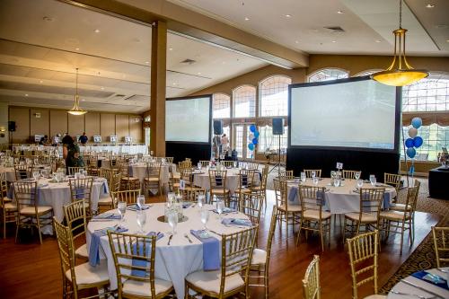 A ballroom set up with two large screens with round tables and gold chairs