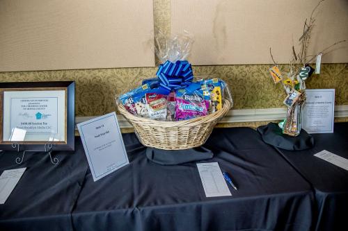 A certificate for family pictures in a frame on the left, then a sign with information about a silent auction item, a basket filled with items and a blue ribbon row over the top, to the right there is a group of branches in a vase with gift cards tied to them
