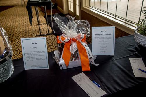 Two signs with information about Silent Auction items set up on a table with a black tablecloth and a white basket with an orange and a white ribbon bow between the signs
