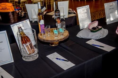 A display with a wooden tray holding multiple bottles of ice wine and tasting glasses on a black tablecloth with a display of sunglasses in a case next to it