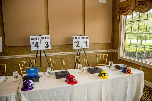 a table with white table cloth with colored plastic jockey hats sitting in front an money boxes behind. Signs on easels in the back have the window numbers 1-4