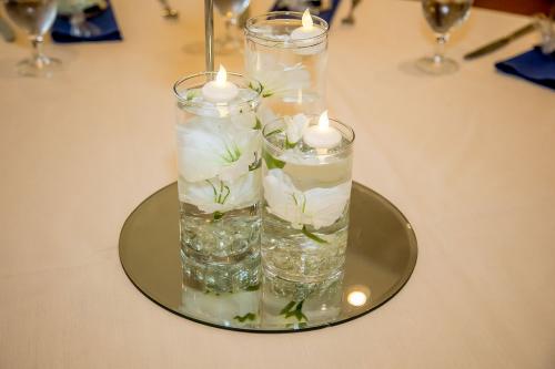three clear cylindrical vases filled with water and floating candles on a round mirror