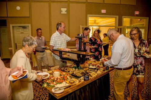 A group of people selecting items from a large, tiered, wooden display of crackers, cheese, dips, and vegetables