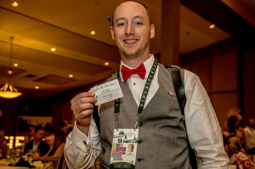 A man in a grey vest with a red bow tie holding up a betting slip