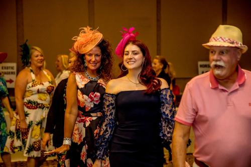 A man and several women parading through the ballroom wearing Derby hats