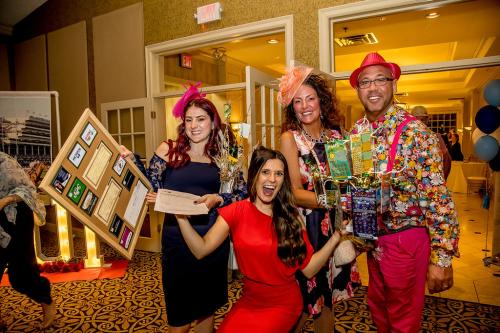 A group of three women and a man holding up the items they won from the Silent Auction